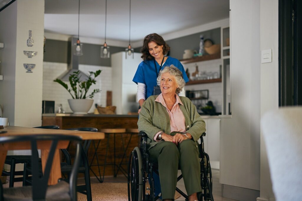 A home health care aide pushes a senior woman in a wheelchair in her home.