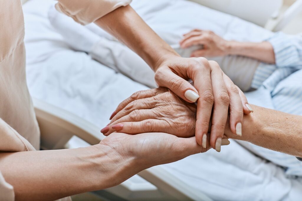 A woman holds the hand of a loved one in hospice care. 