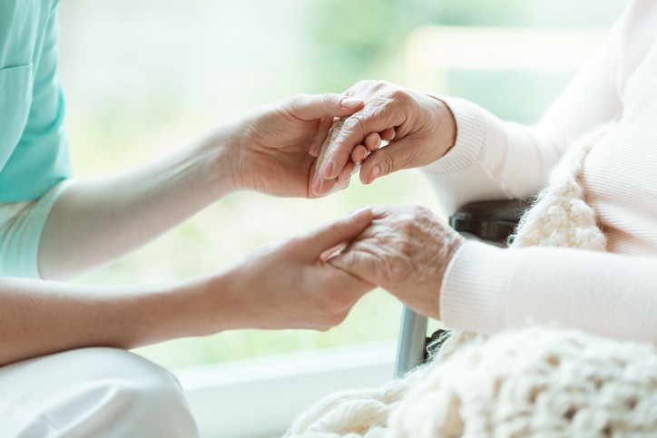 A palliative care nurse holds the hands of a patient.