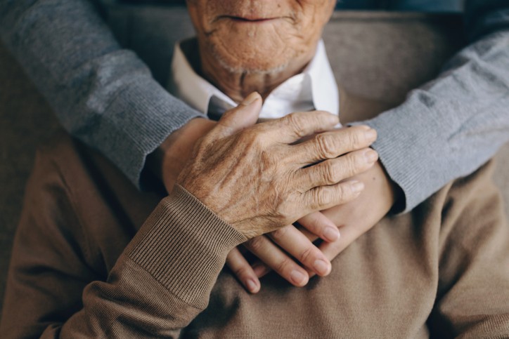 Close up of a family members hands holding an elderly patient from behind.